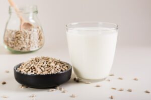 Organic sunflower milk in a glass and seeds in a bowl on the table. Dairy-free alternative