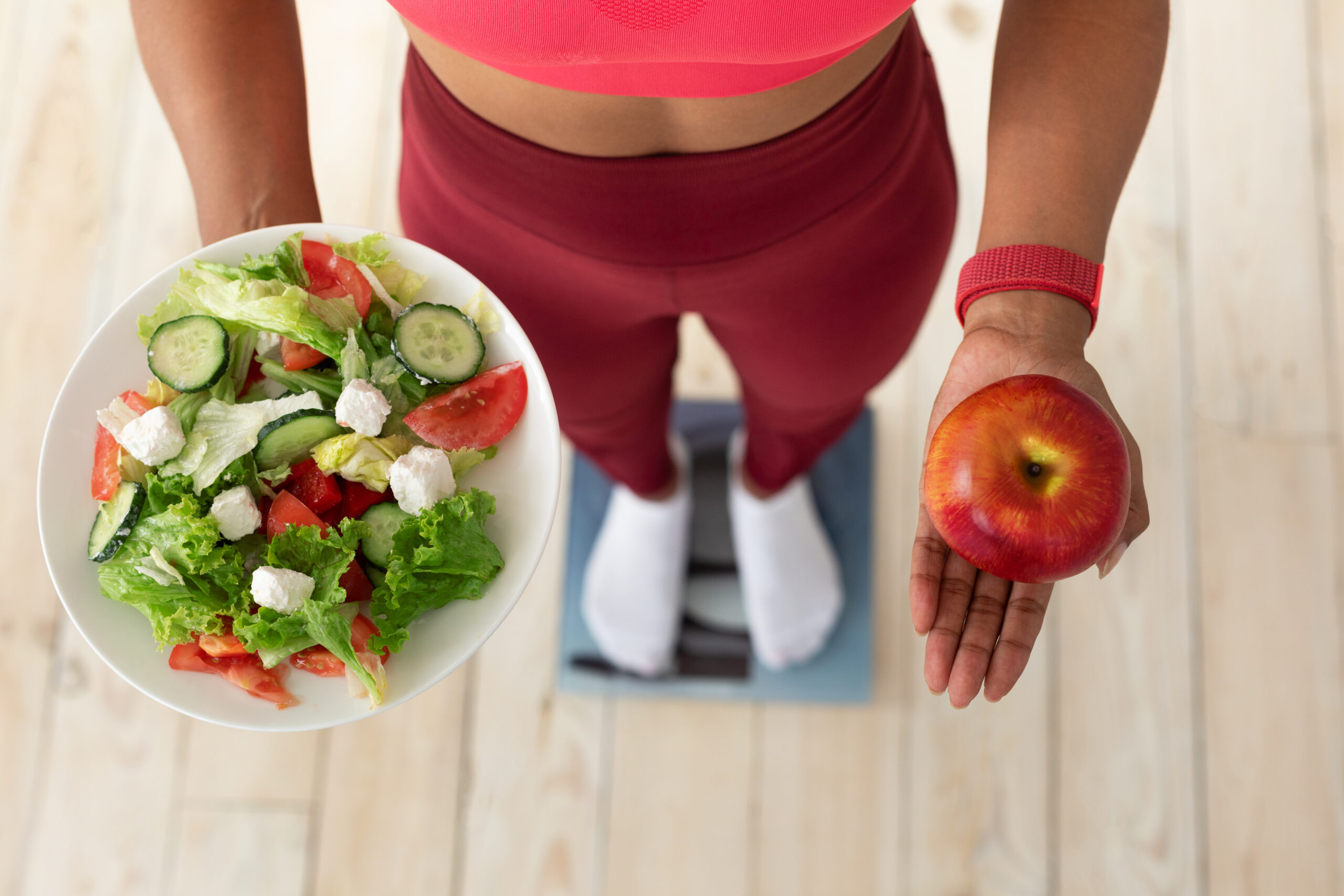 woman standing on scales holding salad and apple i 2022 12 16 08 25 48 utc scaled